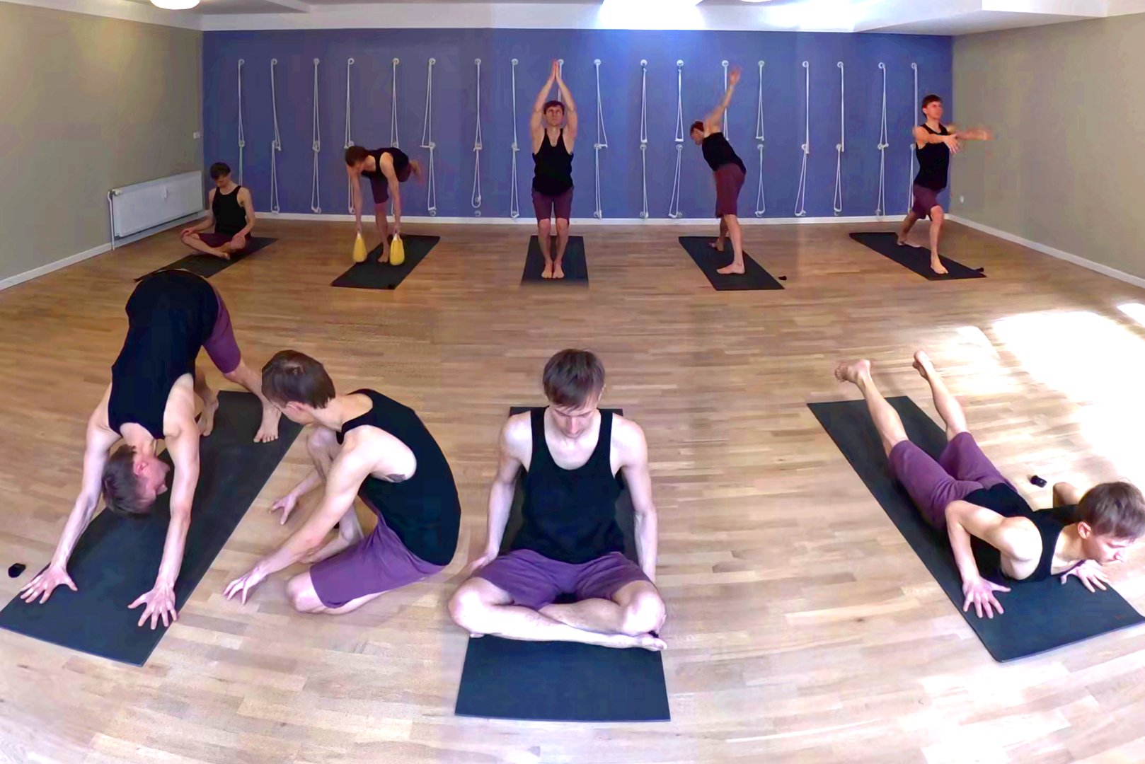 Multiple instances of one and the same person inside a yoga room, exercising various postures.