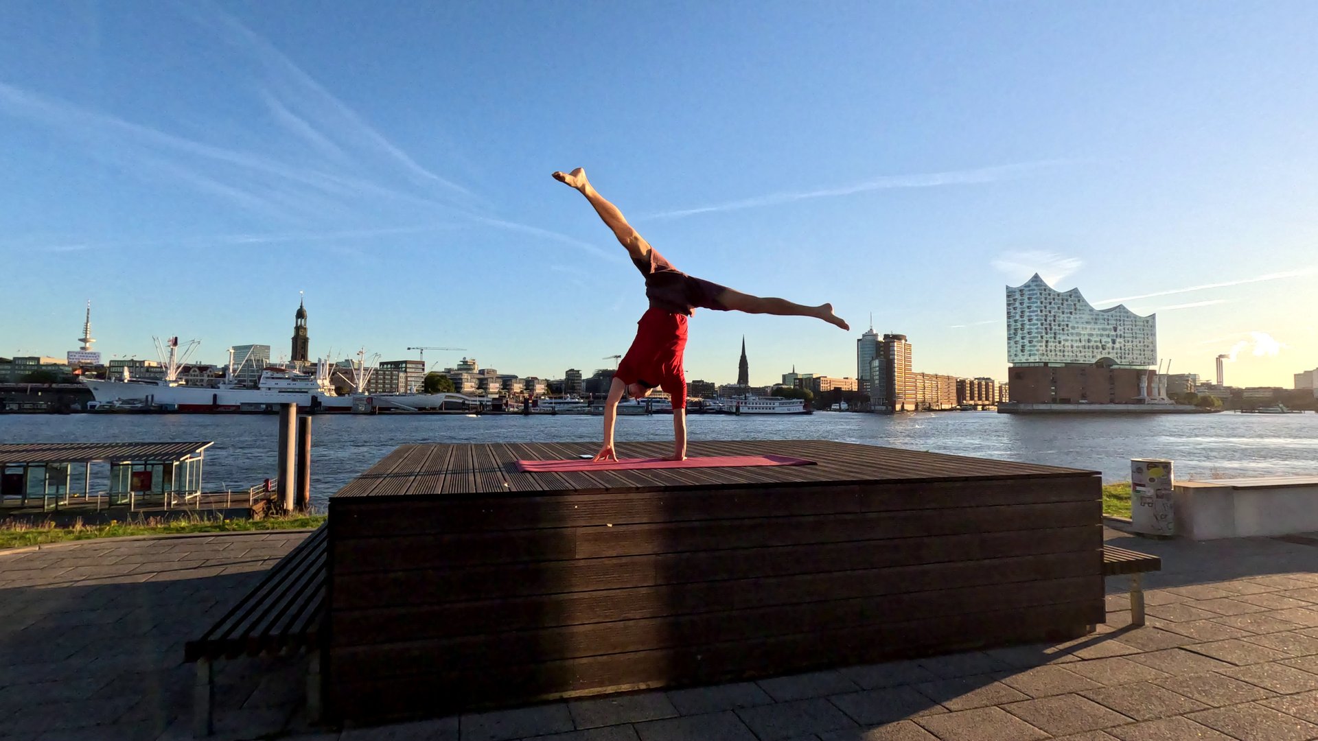 A person performing a one-armed handstand in front of Hamburg's skyline.